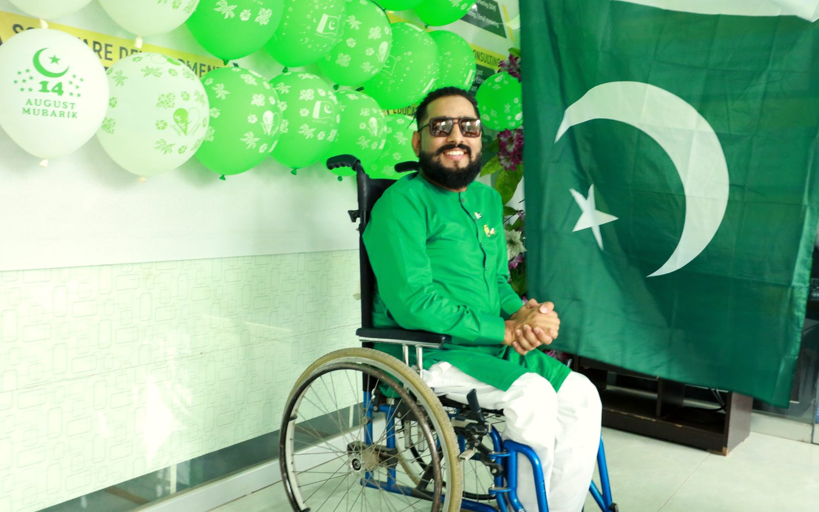Raheel Nawaz in green beside the Pakistan flag on Independence Day